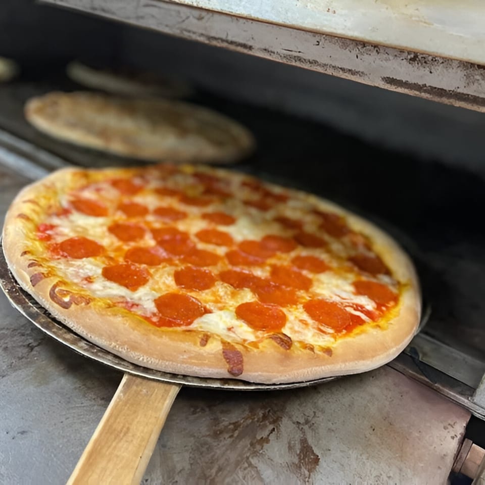 Speedy's Pizza pepperoni pizza on a peel, ready to be placed into a hot oven.