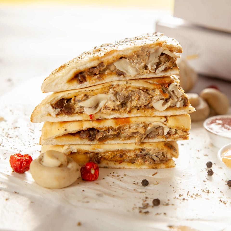 A stack of four Speedy's Pizza calzone slices, filled with meat and cheese, on a white surface.