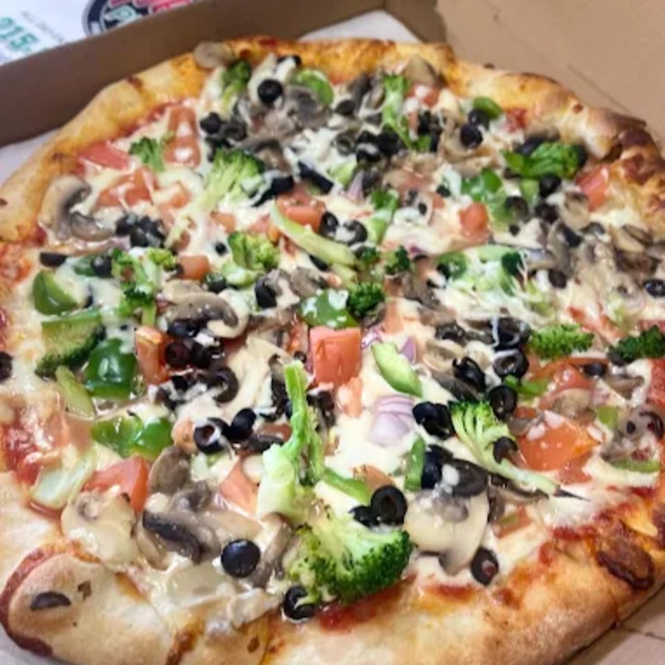 A Speedy's Pizza with broccoli, mushrooms, black olives, green peppers, and tomatoes in a box.