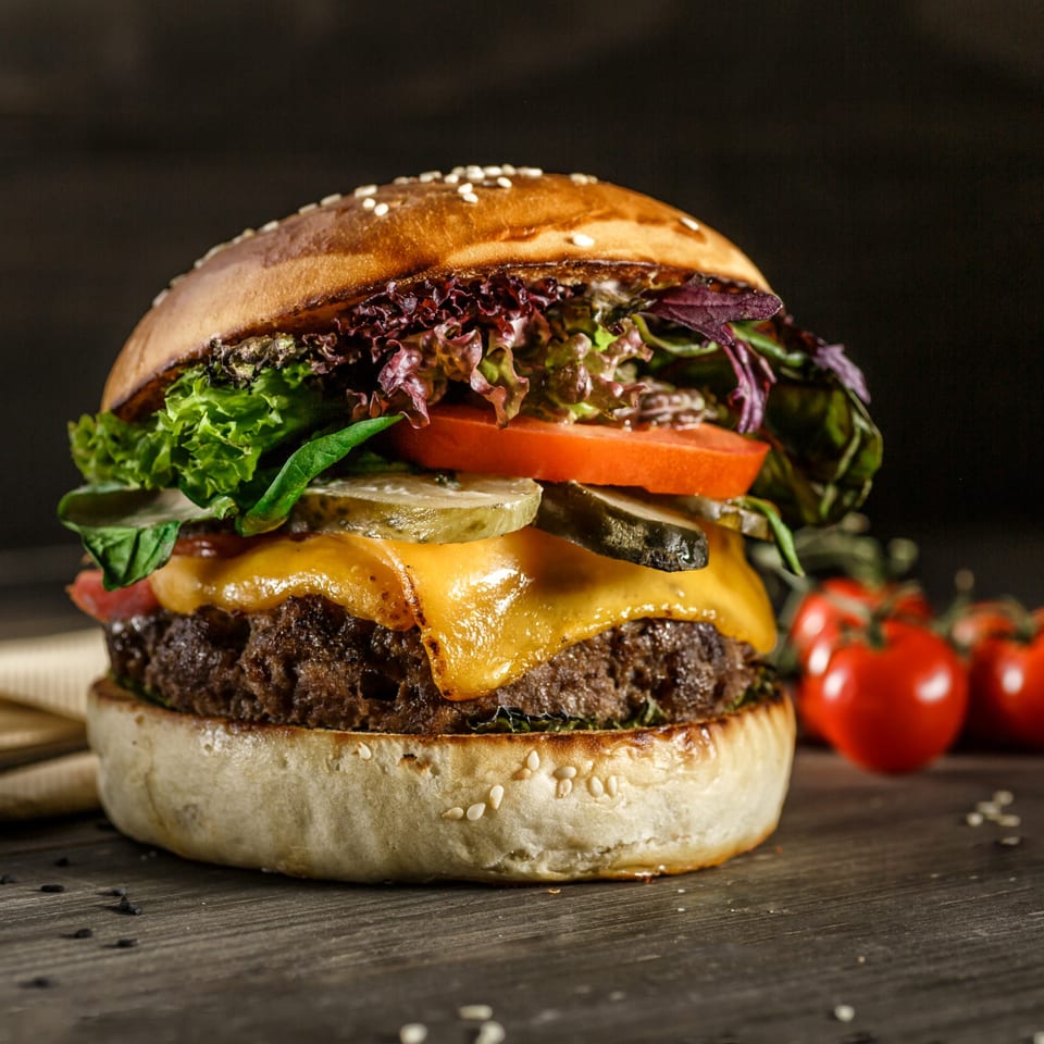 Close-up of a juicy burger with melted cheese, lettuce, tomato, and pickles on a wooden surface.